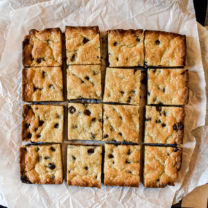 Overhead view of square chocolate chip cookie bars arranged in a grid on parchment paper