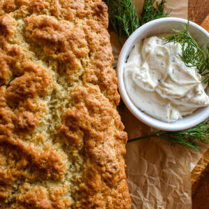 Golden brown freshly baked bread loaf served with a small bowl of herb dip and fresh dill sprigs