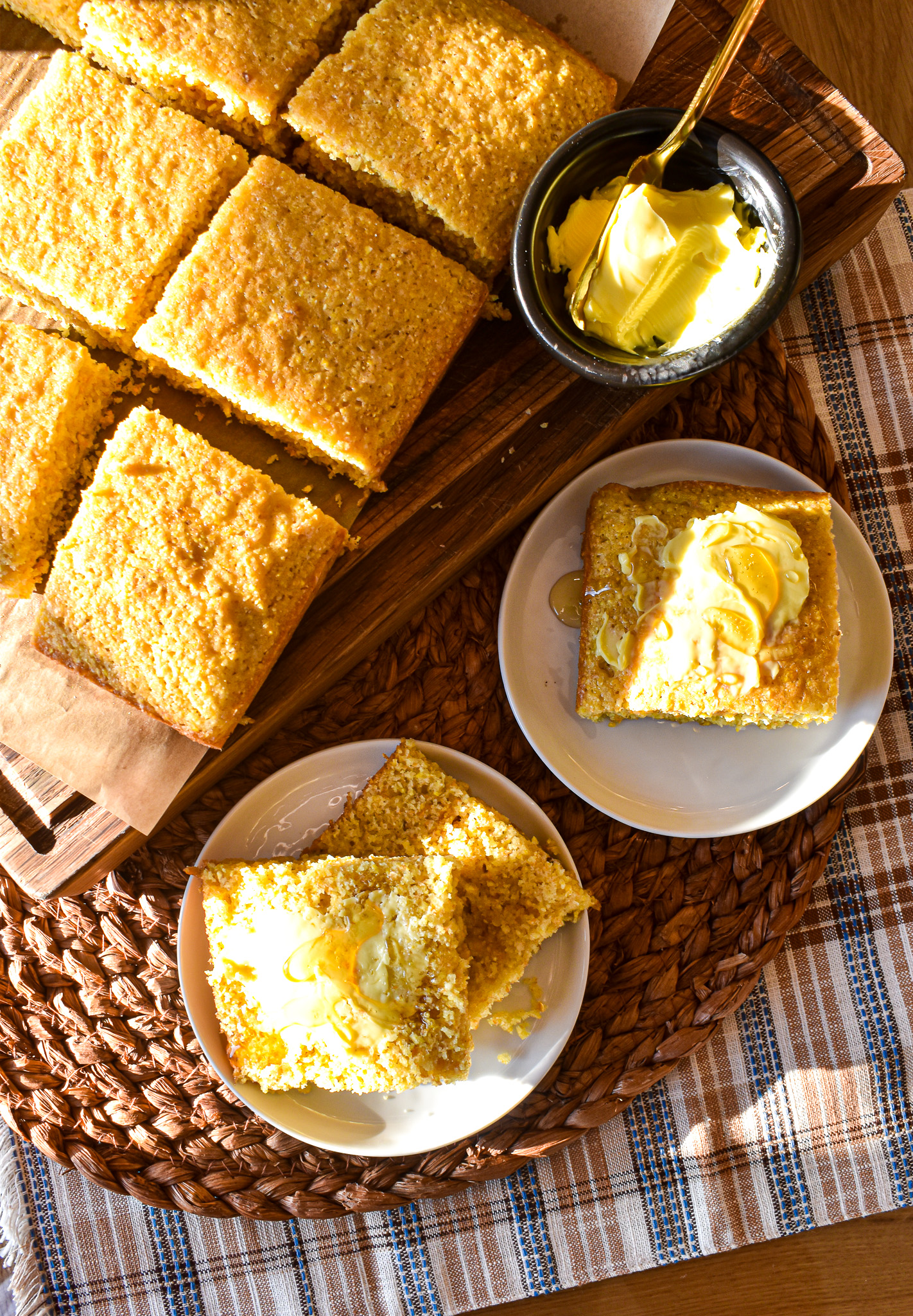 Golden cornbread squares on a wooden cutting board, served with butter and honey