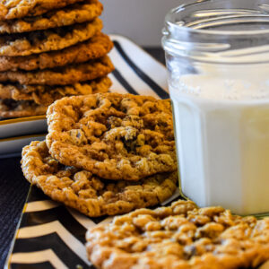 Oatmeal raisin cookies stacked high and spread out on a patterned tray next to a glass of milk