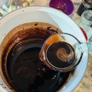 A glass measuring cup holding chocolate milk concentrate scooped from a large white pot