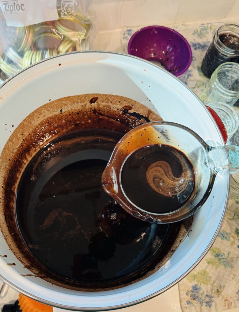 A glass measuring cup holding chocolate milk concentrate scooped from a large white pot